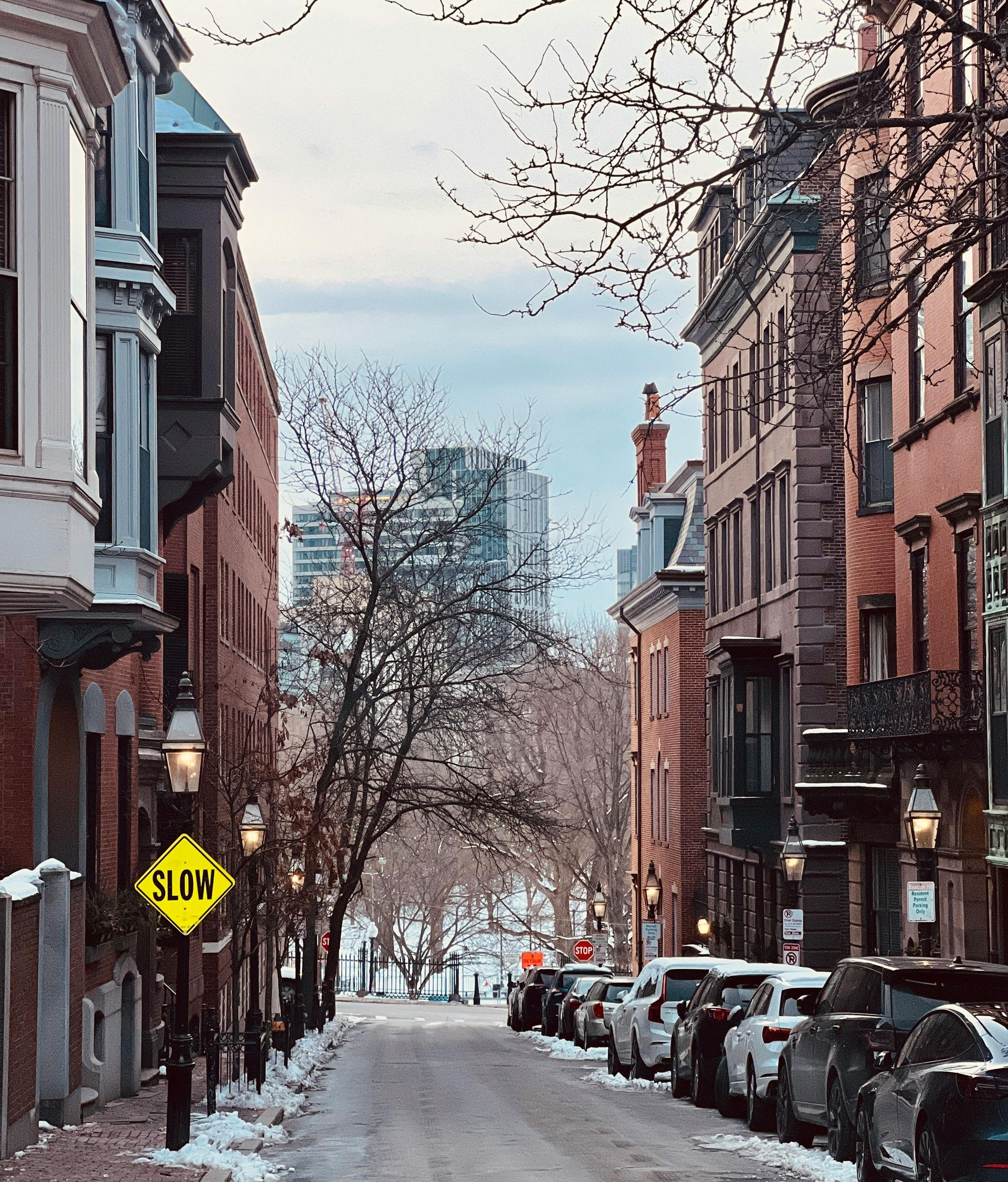 Snowy city street lined with brick buildings, parked cars, and a