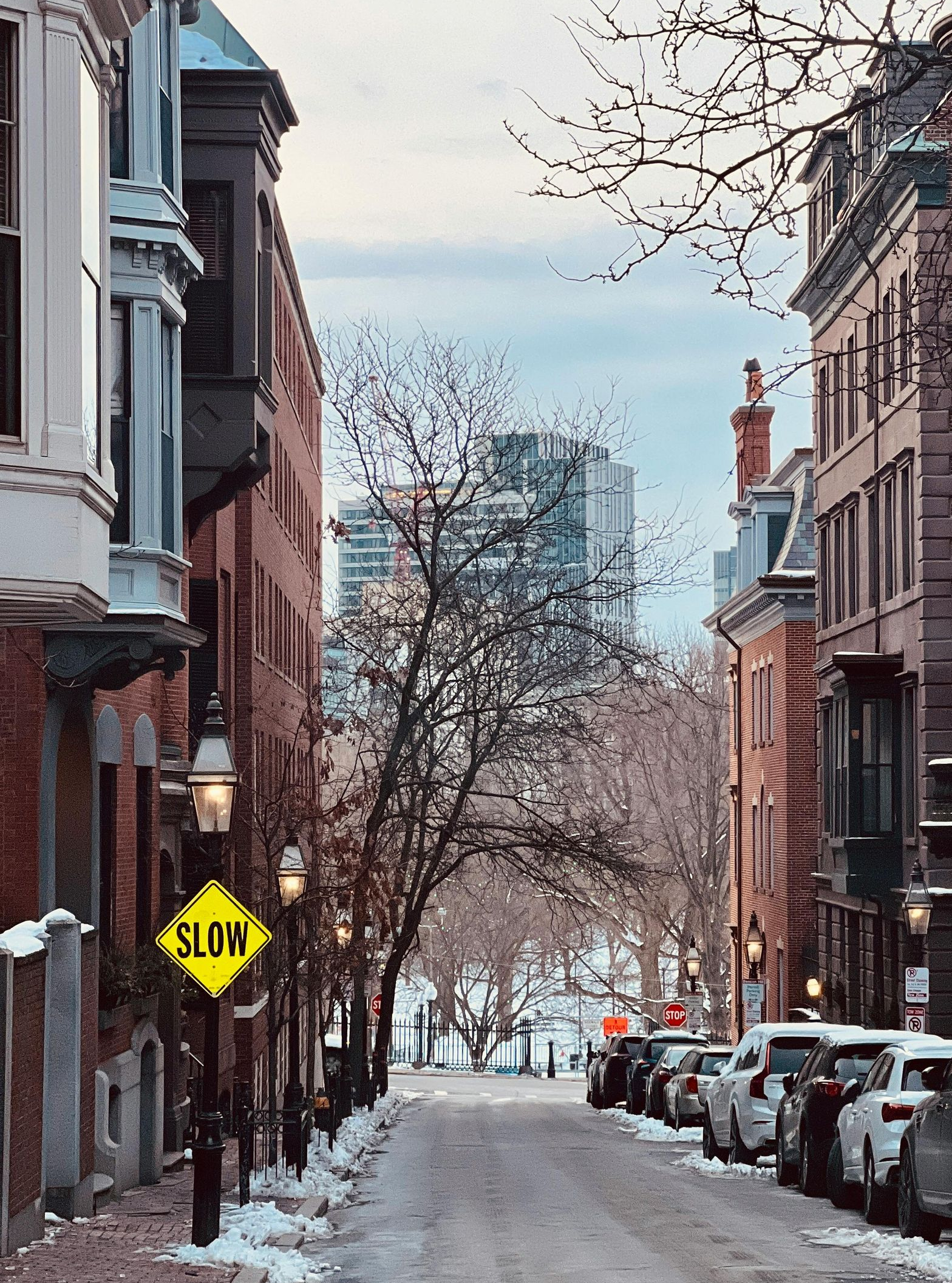 Snowy city street lined with brick buildings, parked cars, and a