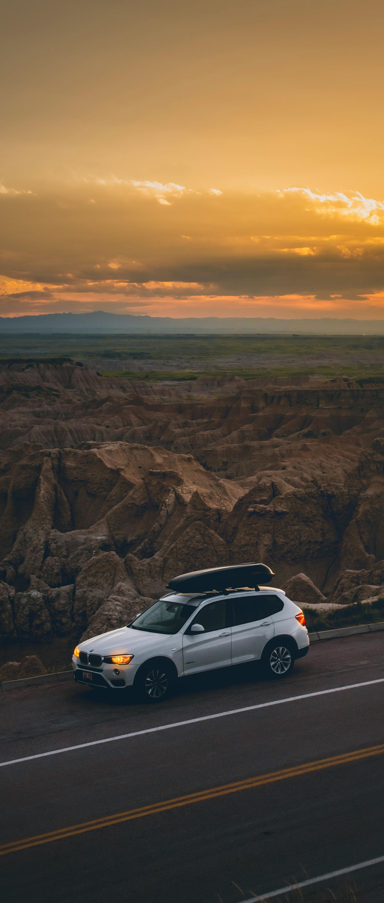 White SUV parked on a roadside overlooking a canyon at sunset.
