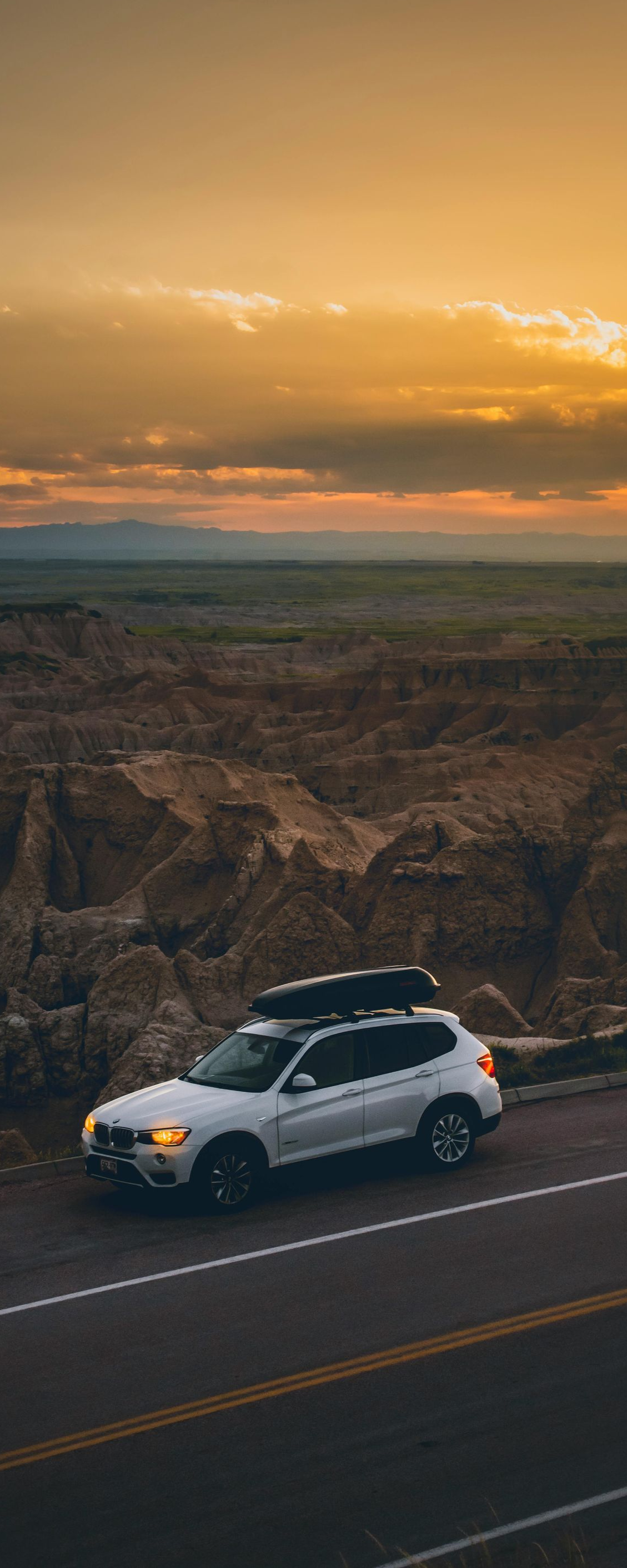 White SUV parked on a roadside overlooking a canyon at sunset.