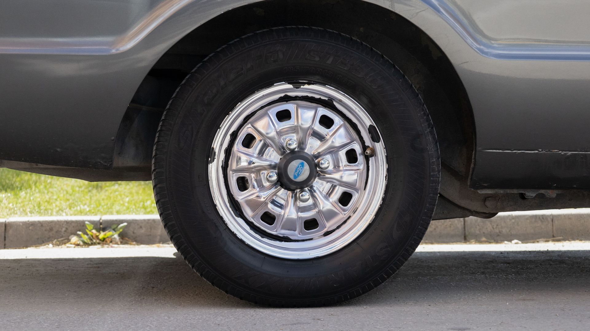 Close-up of a car’s rear wheel and chrome hubcap parked by a curb.