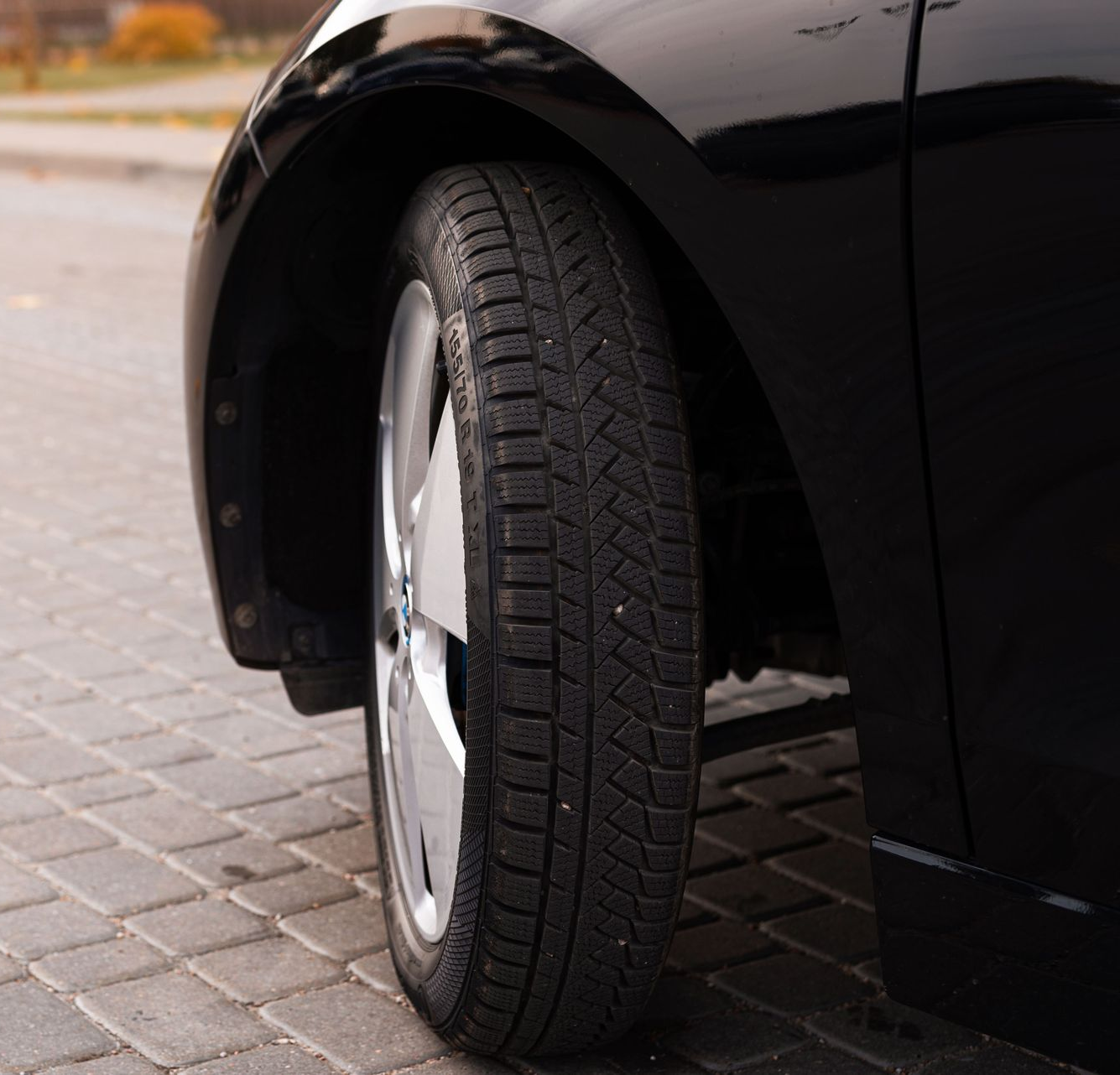 Close-up of a black car’s front wheel parked on a paved street.