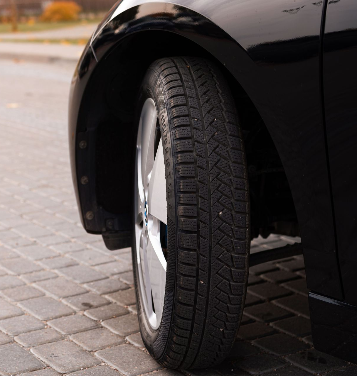 Close-up of a black car’s front wheel parked on a paved street.