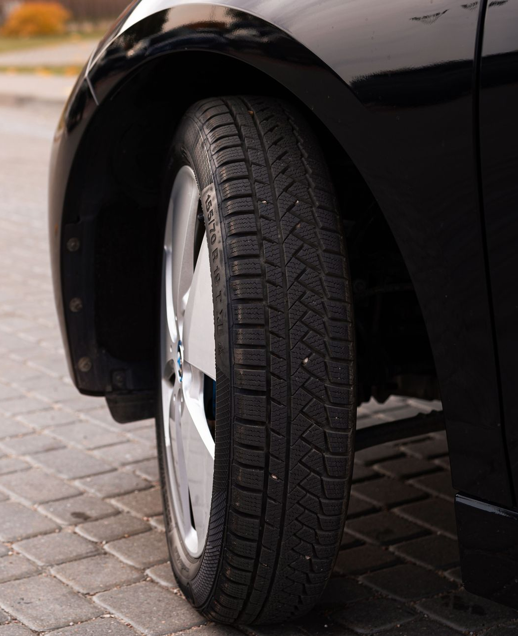 Close-up of a black car’s front wheel parked on a paved street.