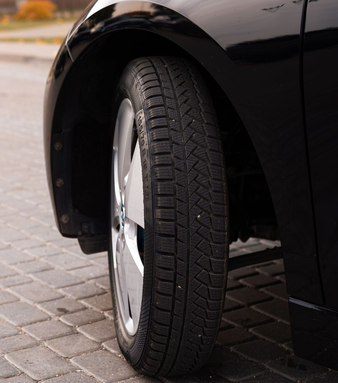 Close-up of a black car’s front wheel parked on a paved street.