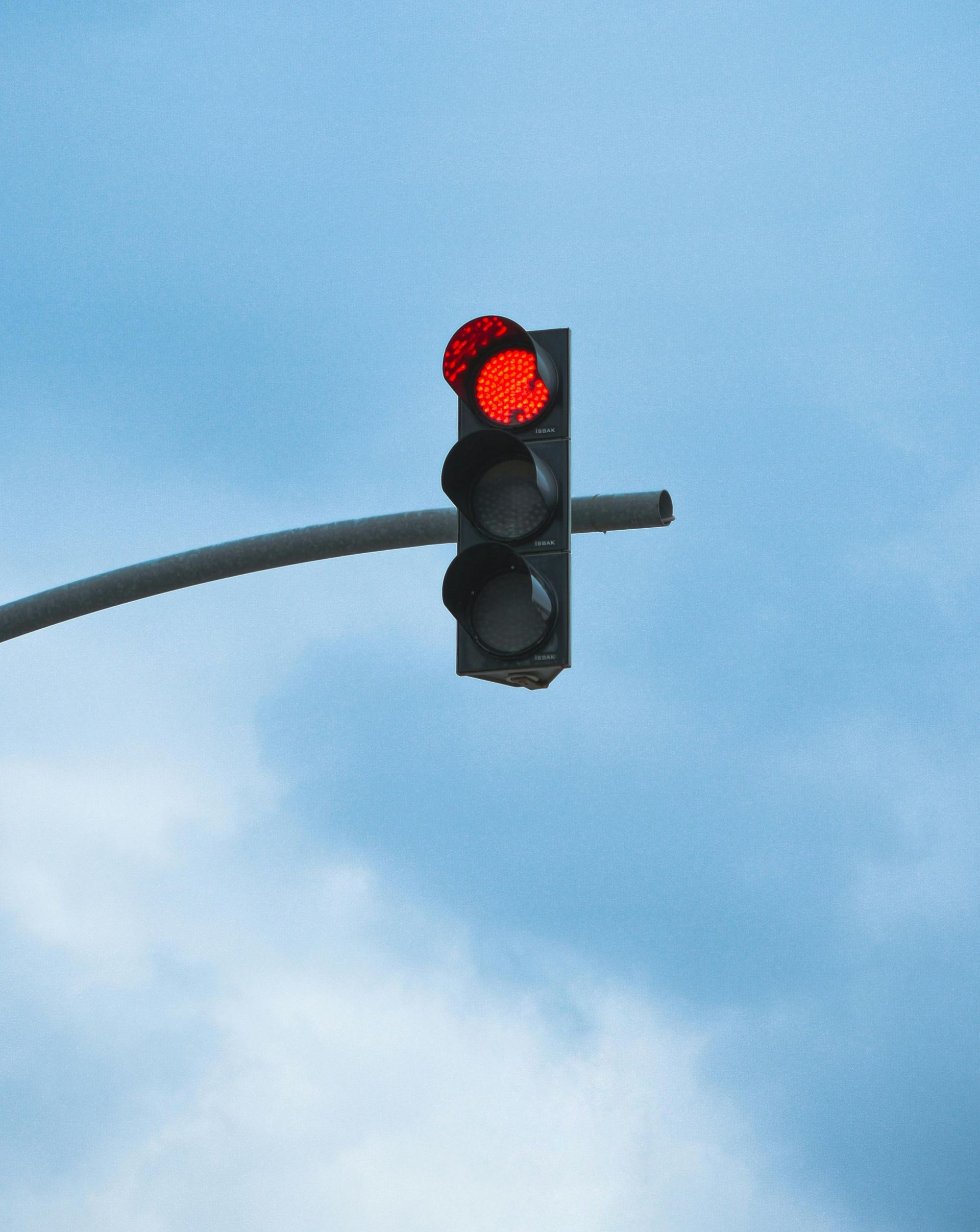 Red traffic light on a pole against a cloudy blue sky.