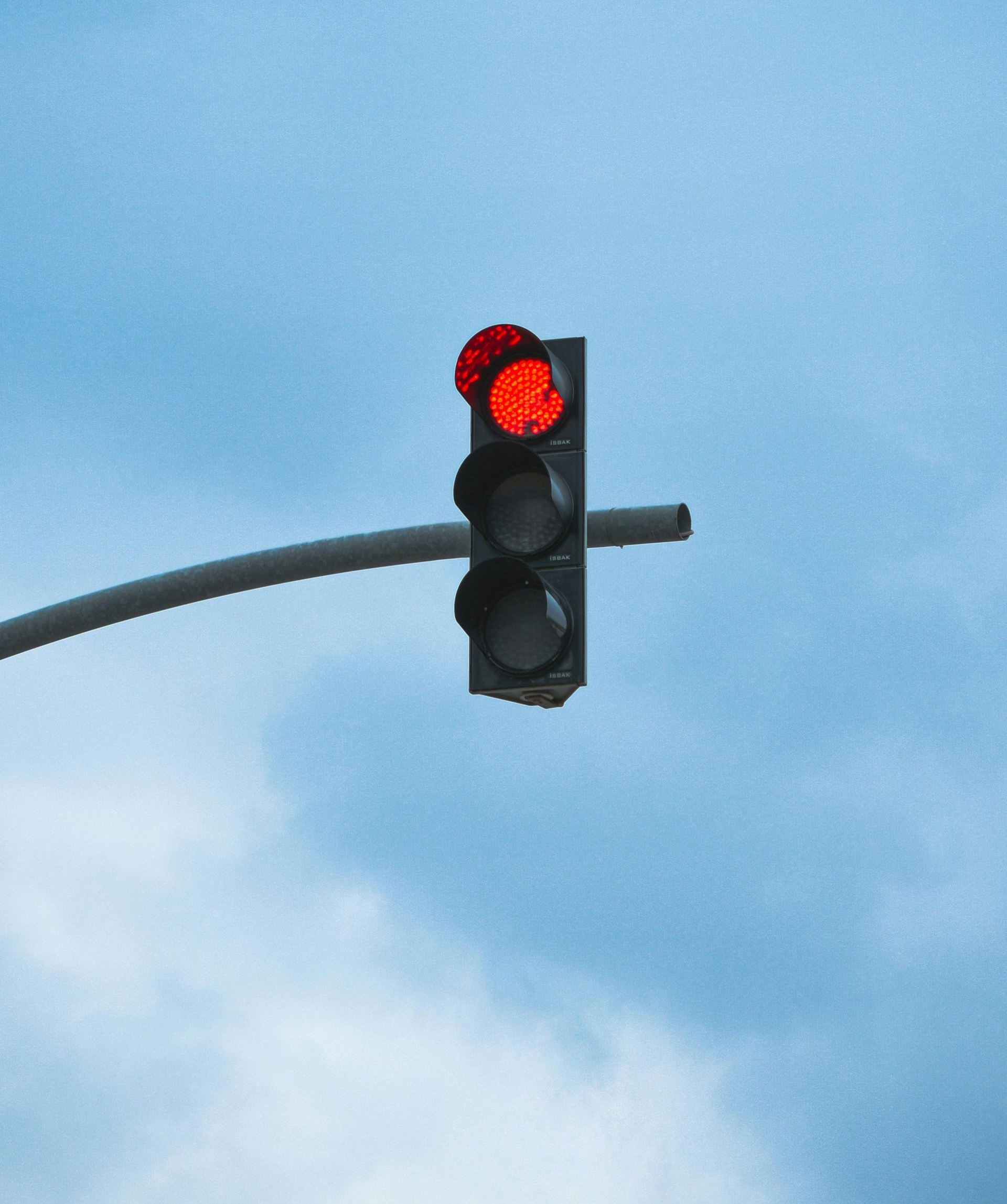 Red traffic light on a pole against a cloudy blue sky.