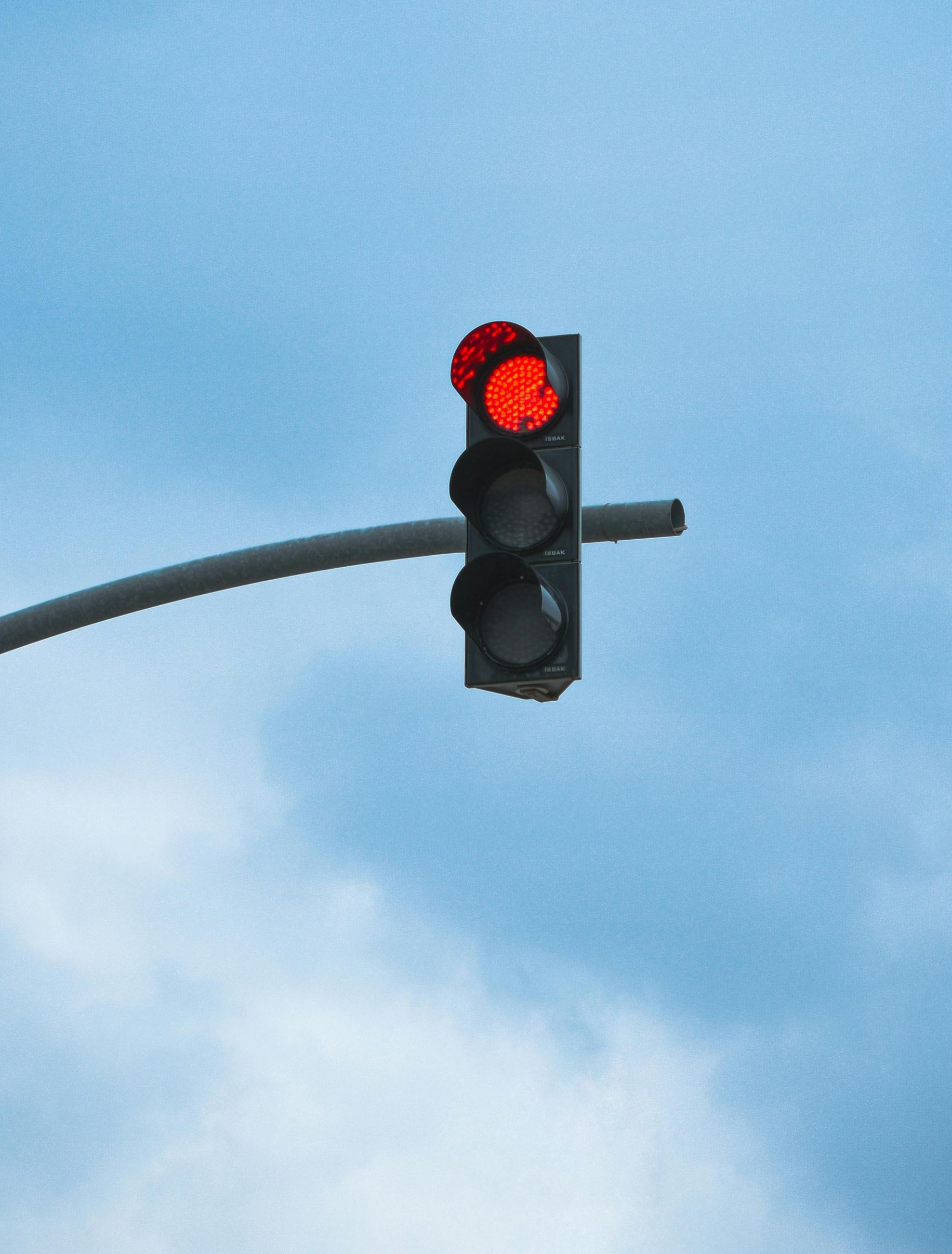 Red traffic light on a pole against a cloudy blue sky.