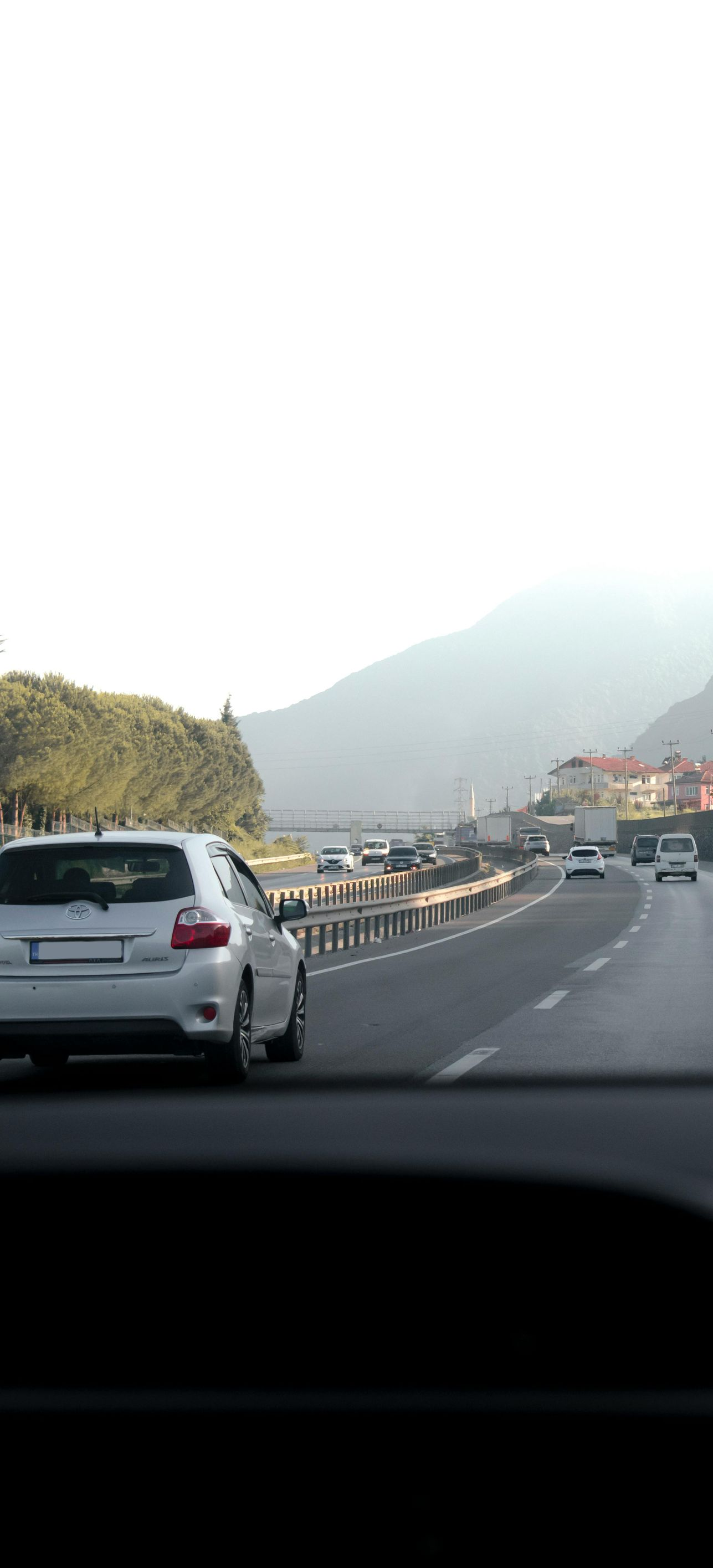 Road view with cars driving toward a hazy mountain under bright sky.