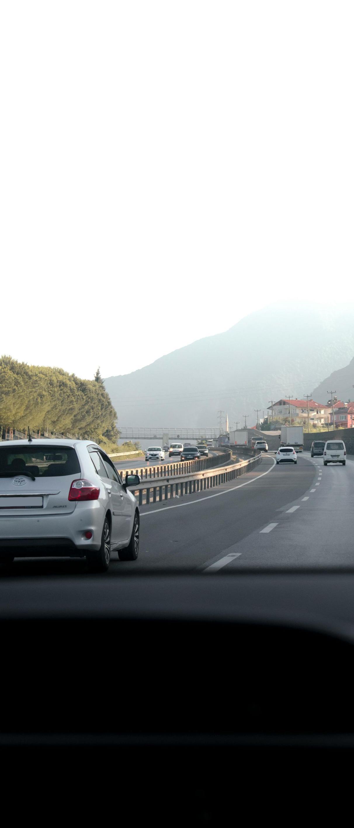 Road view with cars driving toward a hazy mountain under bright sky.