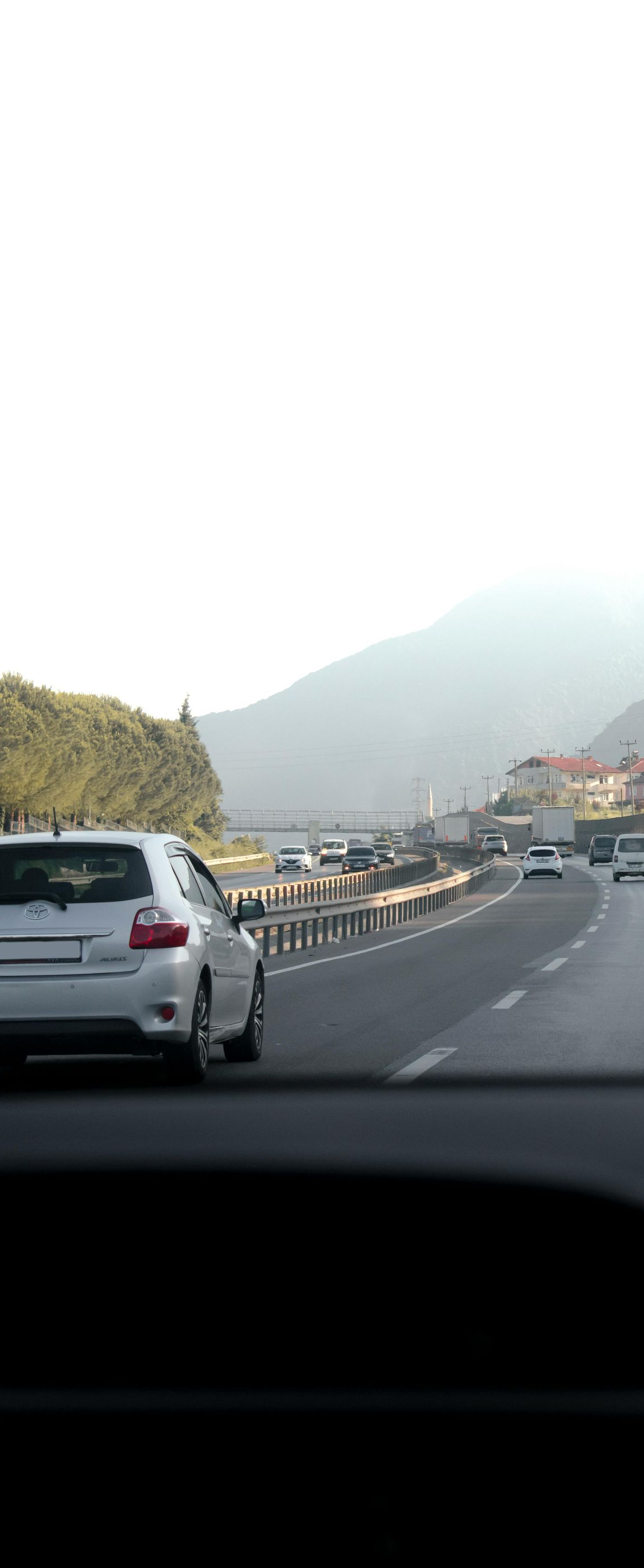 Road view with cars driving toward a hazy mountain under bright sky.