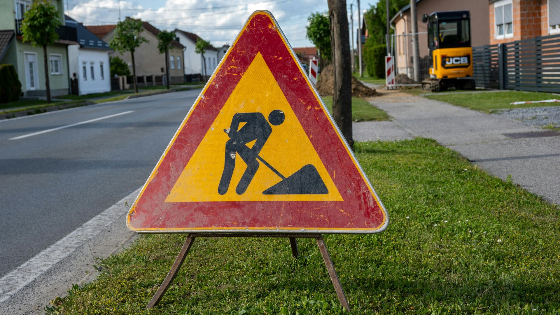 Roadwork warning sign on a grassy roadside in a suburban neighborhood