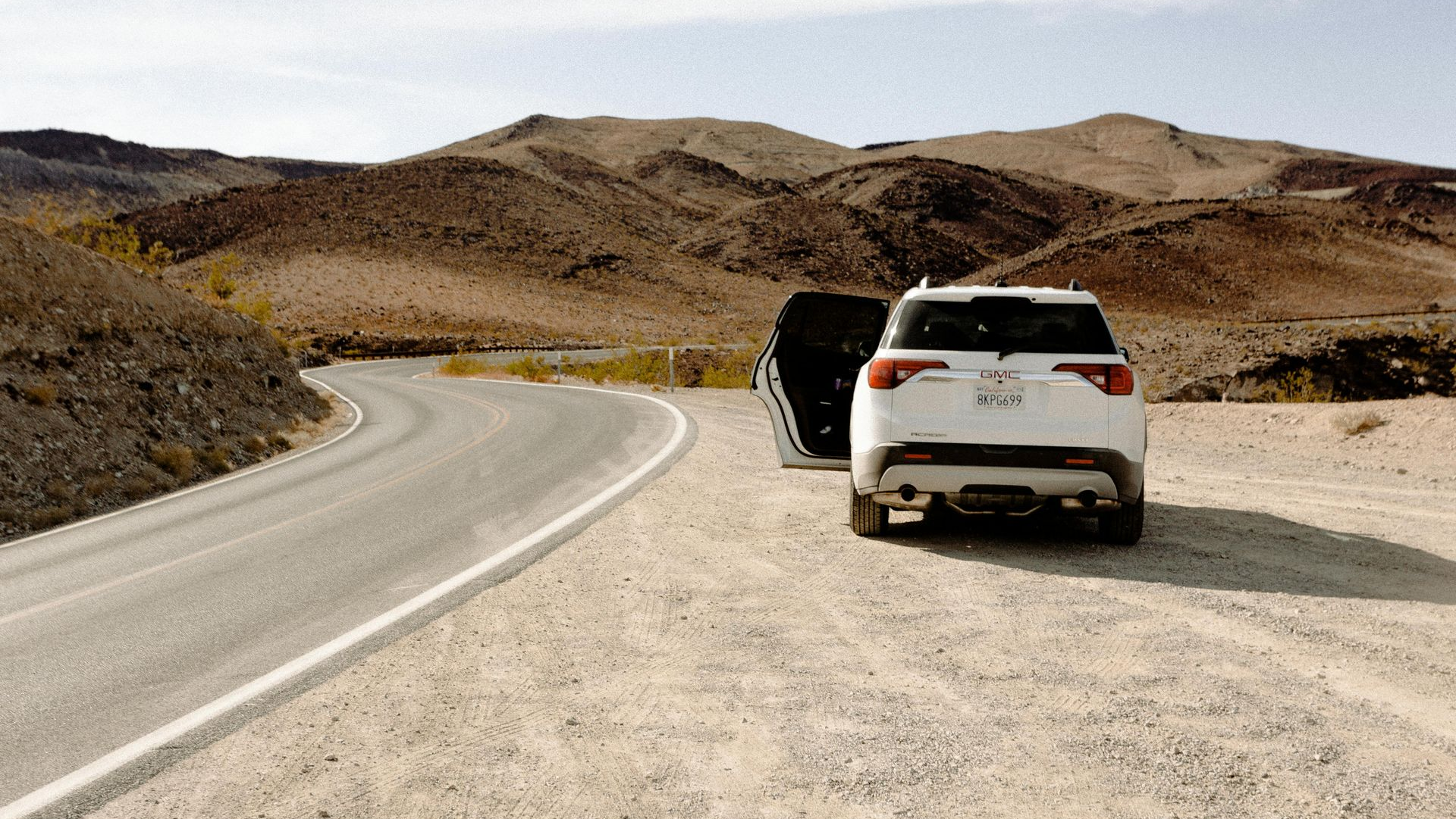 Two SUVs parked on a winding desert road beside rocky hills under a clear sky