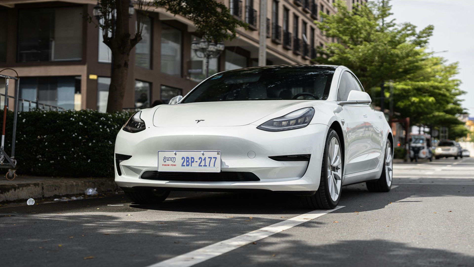 White Tesla parked on a city street beside apartment buildings and trees