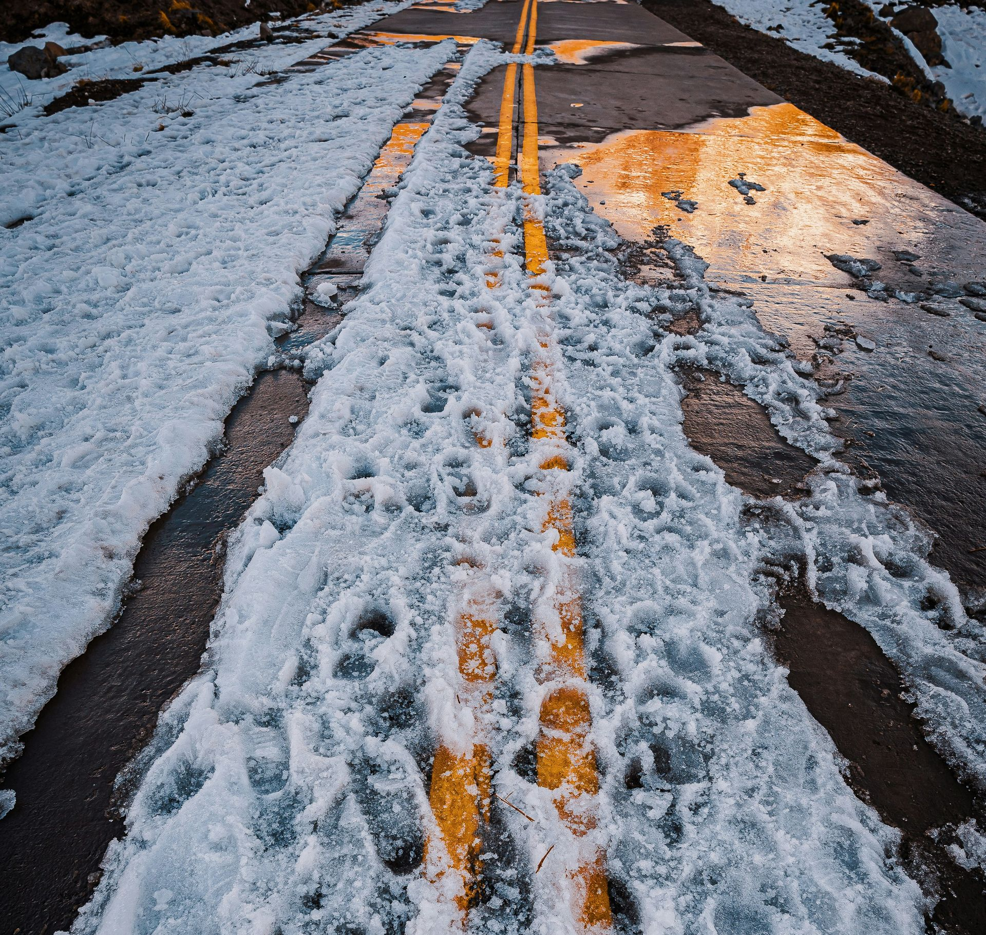Road covered in snow with yellow lines, footprints in the snow.