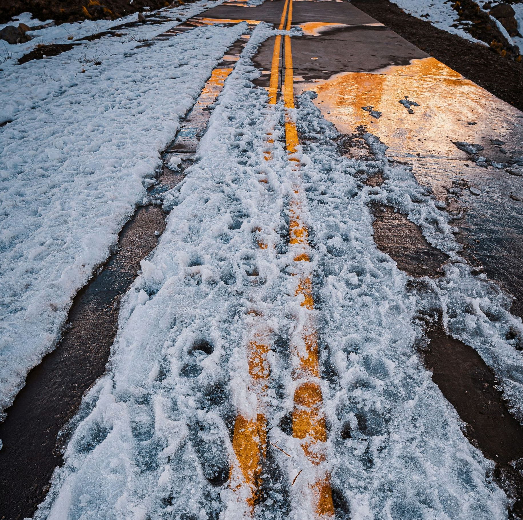 Road covered in snow with yellow lines, footprints in the snow.