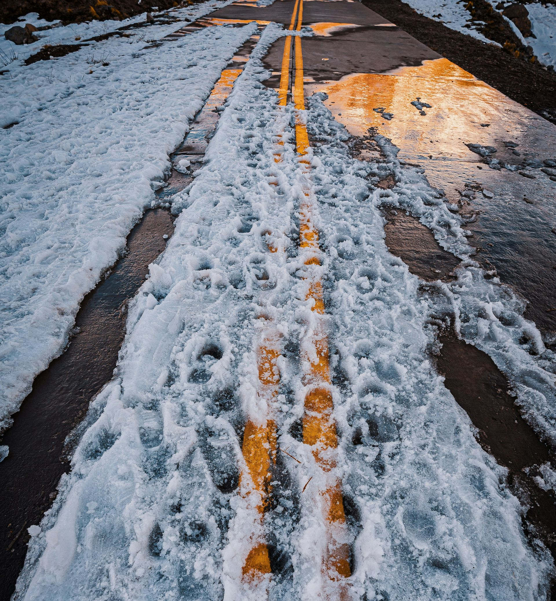 Road covered in snow with yellow lines, footprints in the snow.