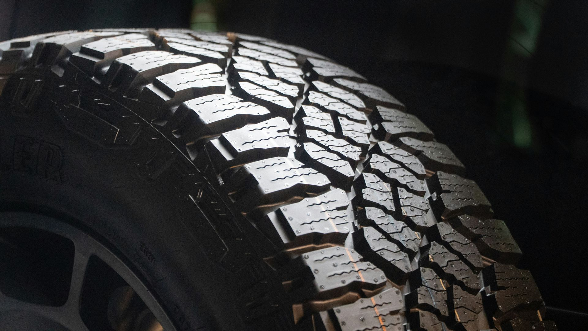 Black tire tread on a vehicle wheel, lit from above, showing rugged pattern.