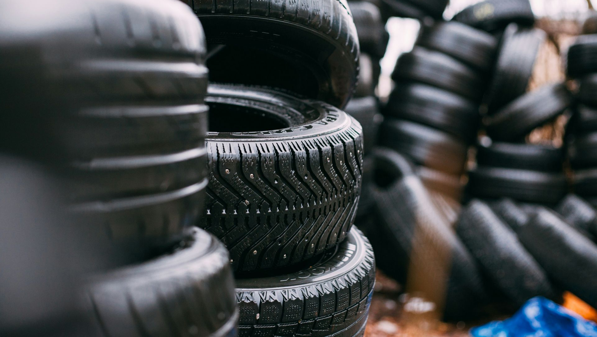 Stacks of black car tires in a tire shop, with one treaded tire centered in the foreground.