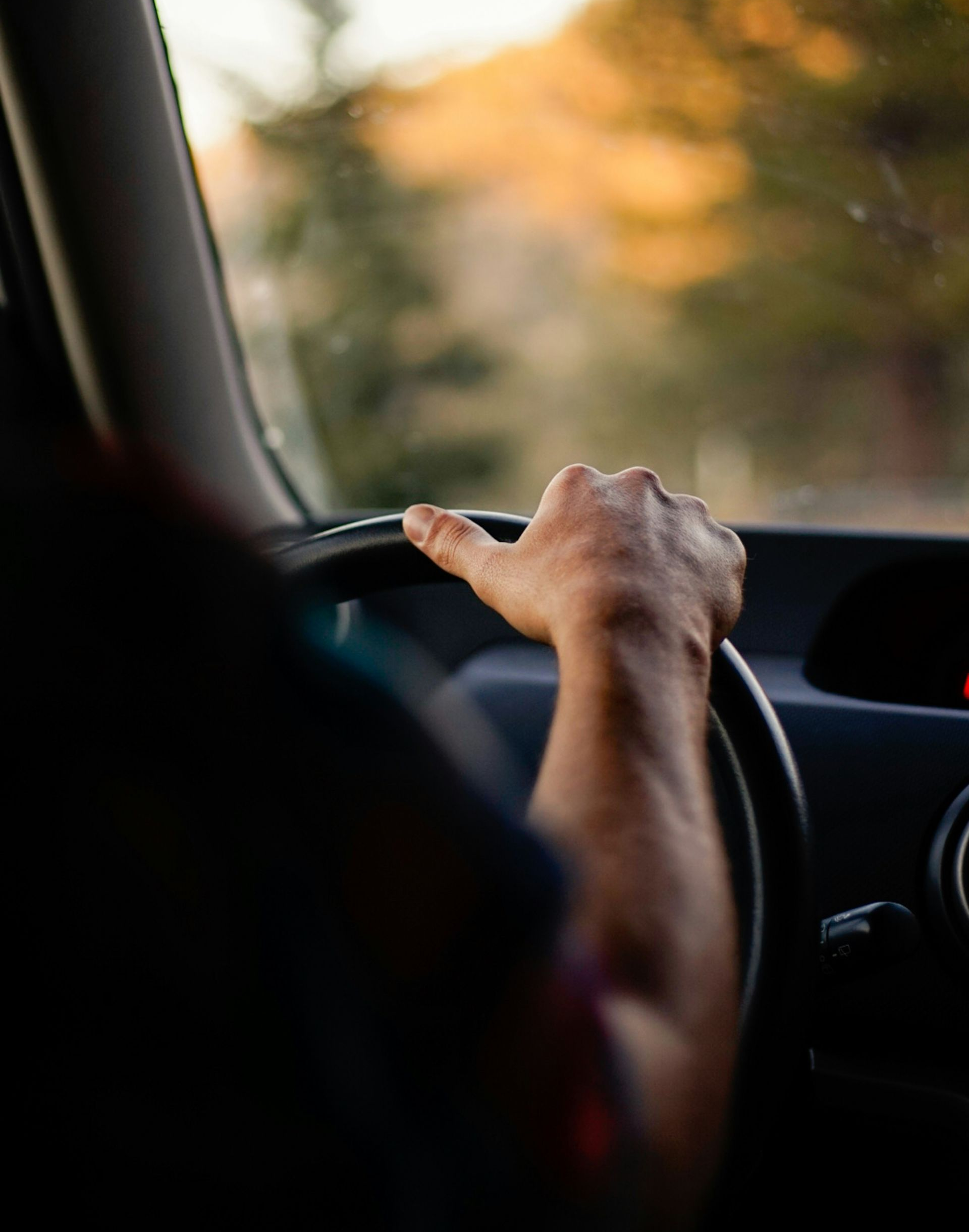 Driver’s hand on steering wheel in a car, with a blurred sunset view ahead.