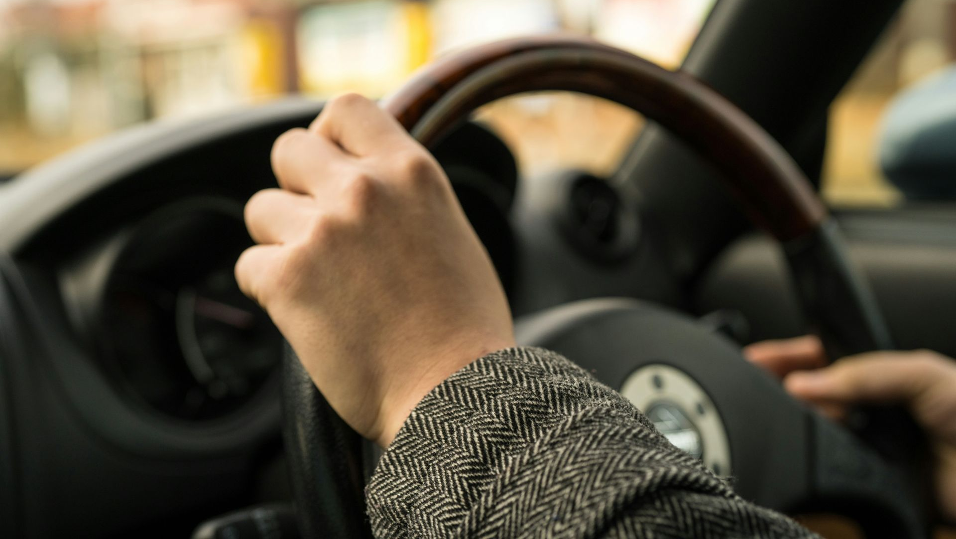 Hand on a steering wheel inside a car, driving in traffic