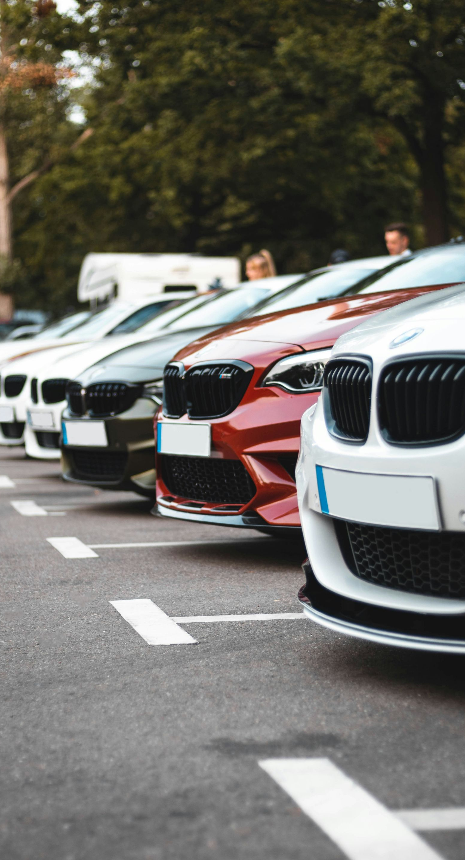 Parked BMW cars lined up along a street, with a white and red car in the foreground.