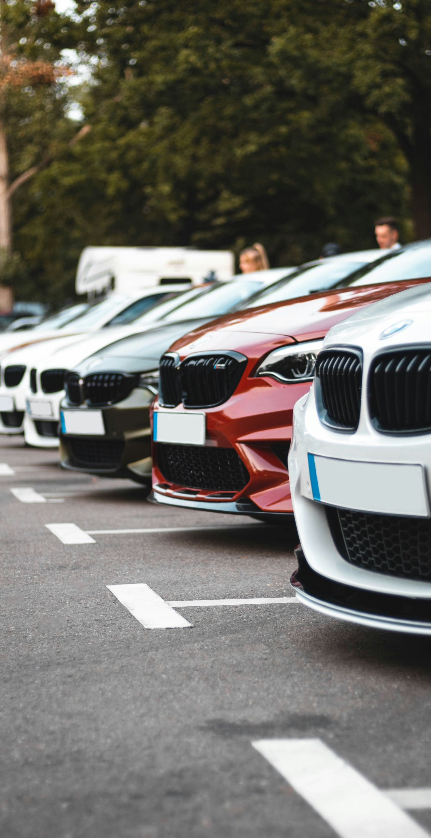 Parked BMW cars lined up along a street, with a white and red car in the foreground.