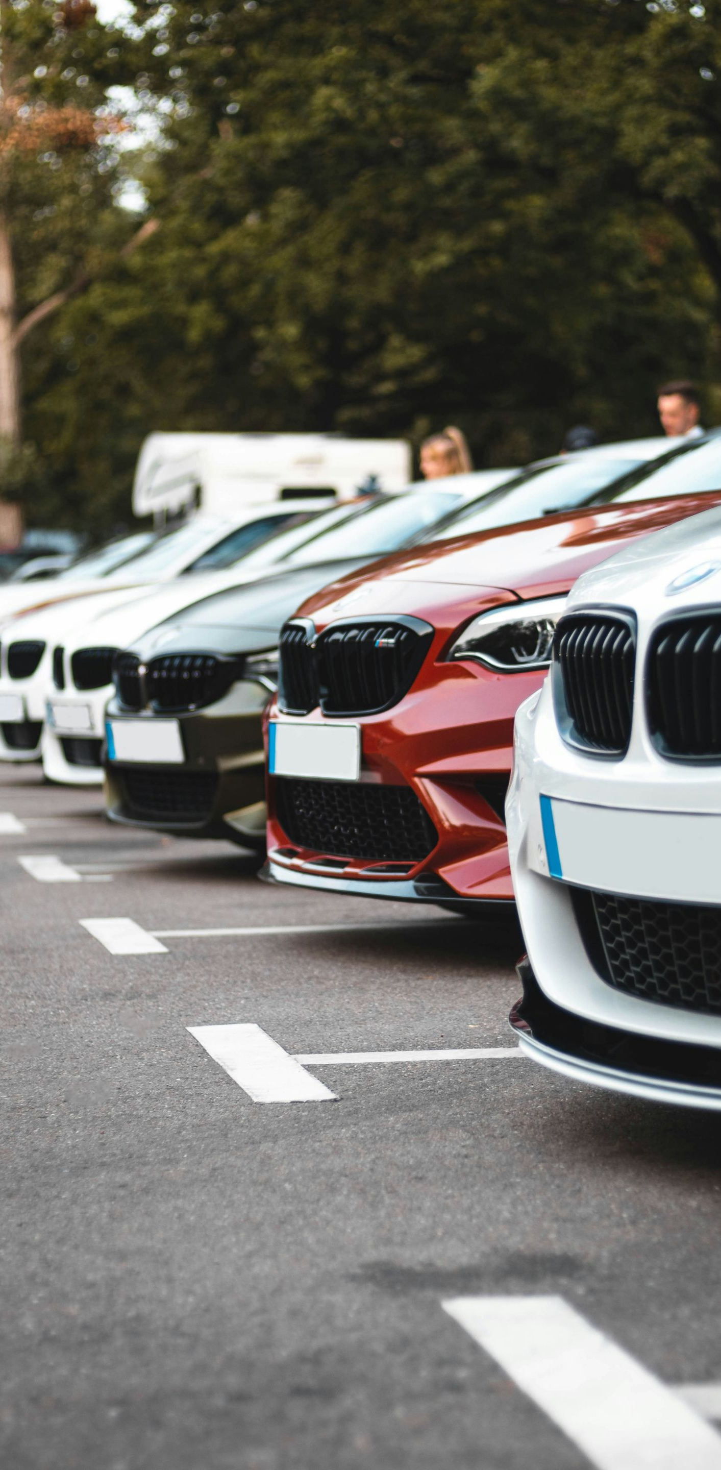 Parked BMW cars lined up along a street, with a white and red car in the foreground.