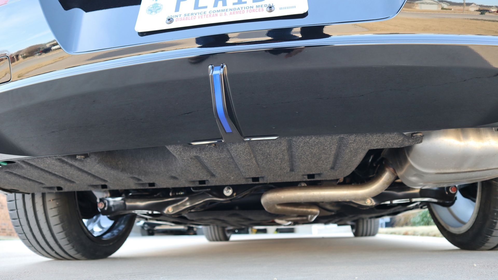 Undercarriage of a blue car showing the exhaust and rear wheels on a driveway.