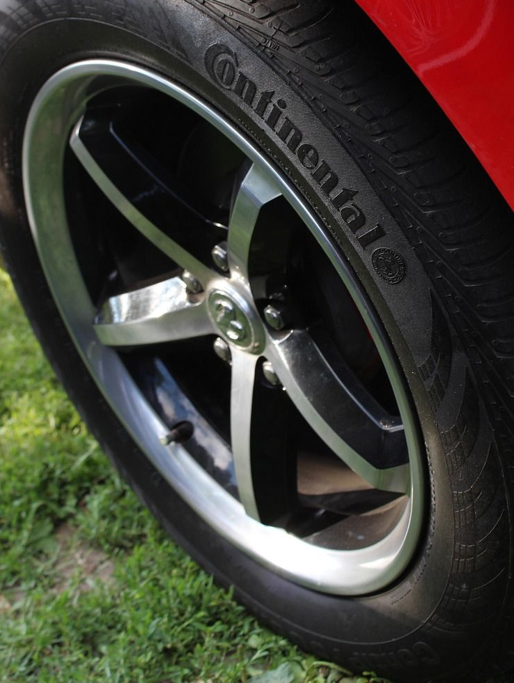 Black and silver car wheel with Continental tire, set on green grass.