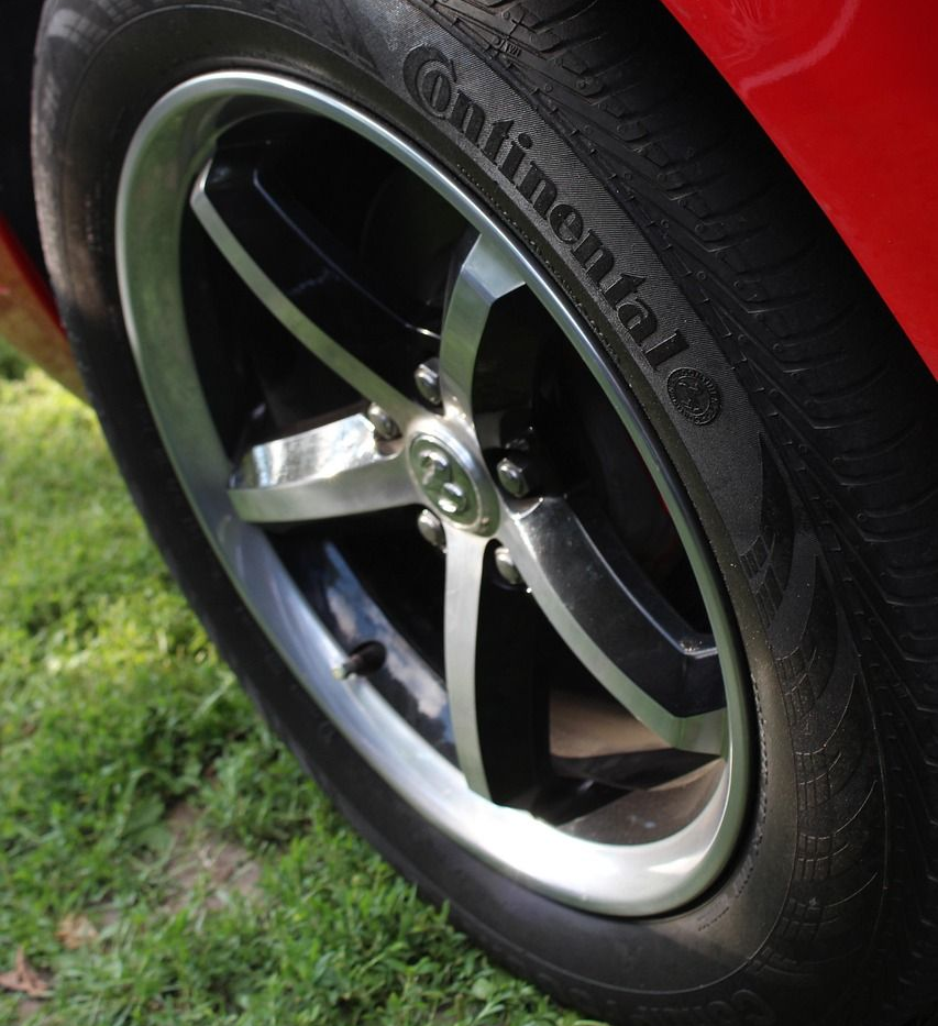 Black and silver car wheel with Continental tire, set on green grass.