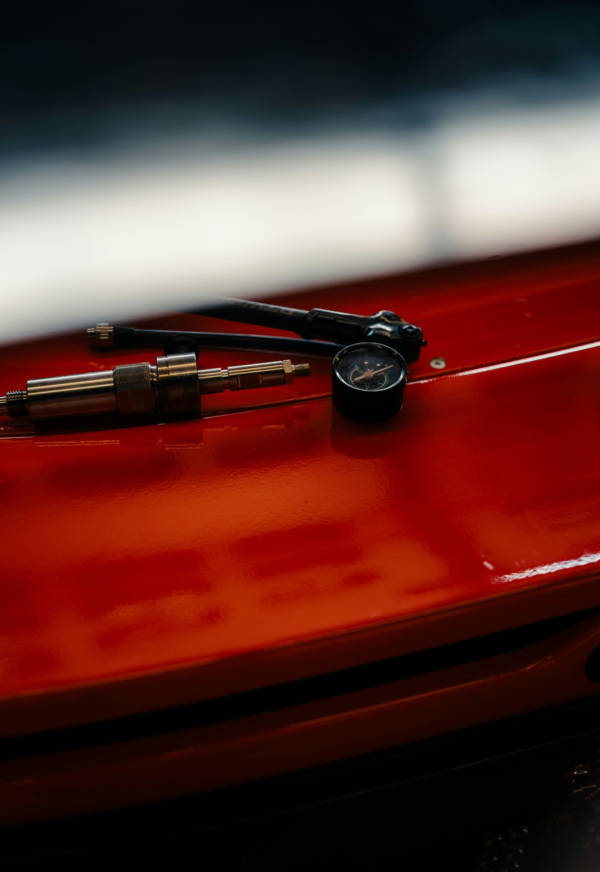 A tire pressure gauge and a valve stem tool rest on the bright red, glossy surface of a car hood.