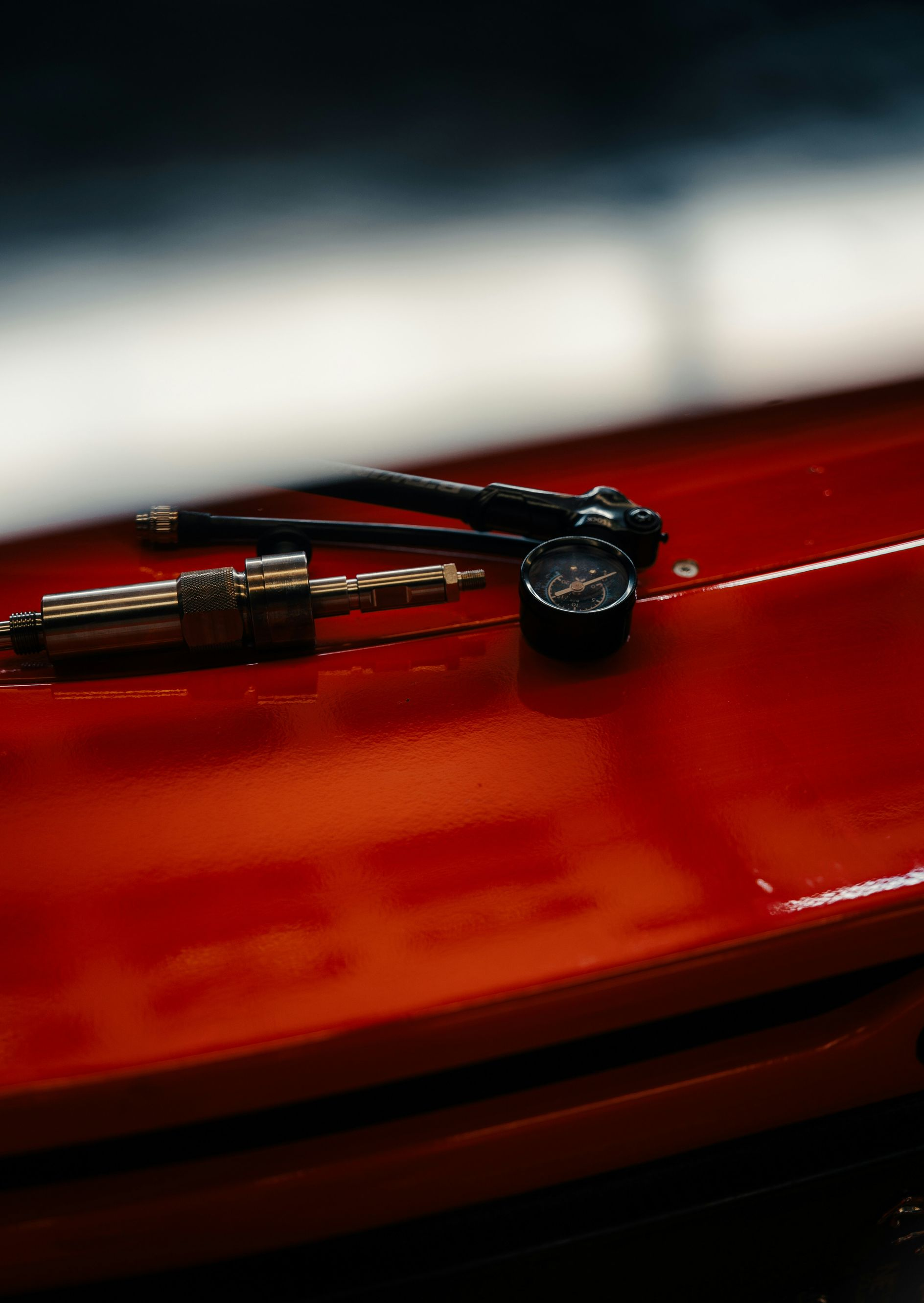A tire pressure gauge and a valve stem tool rest on the bright red, glossy surface of a car hood.