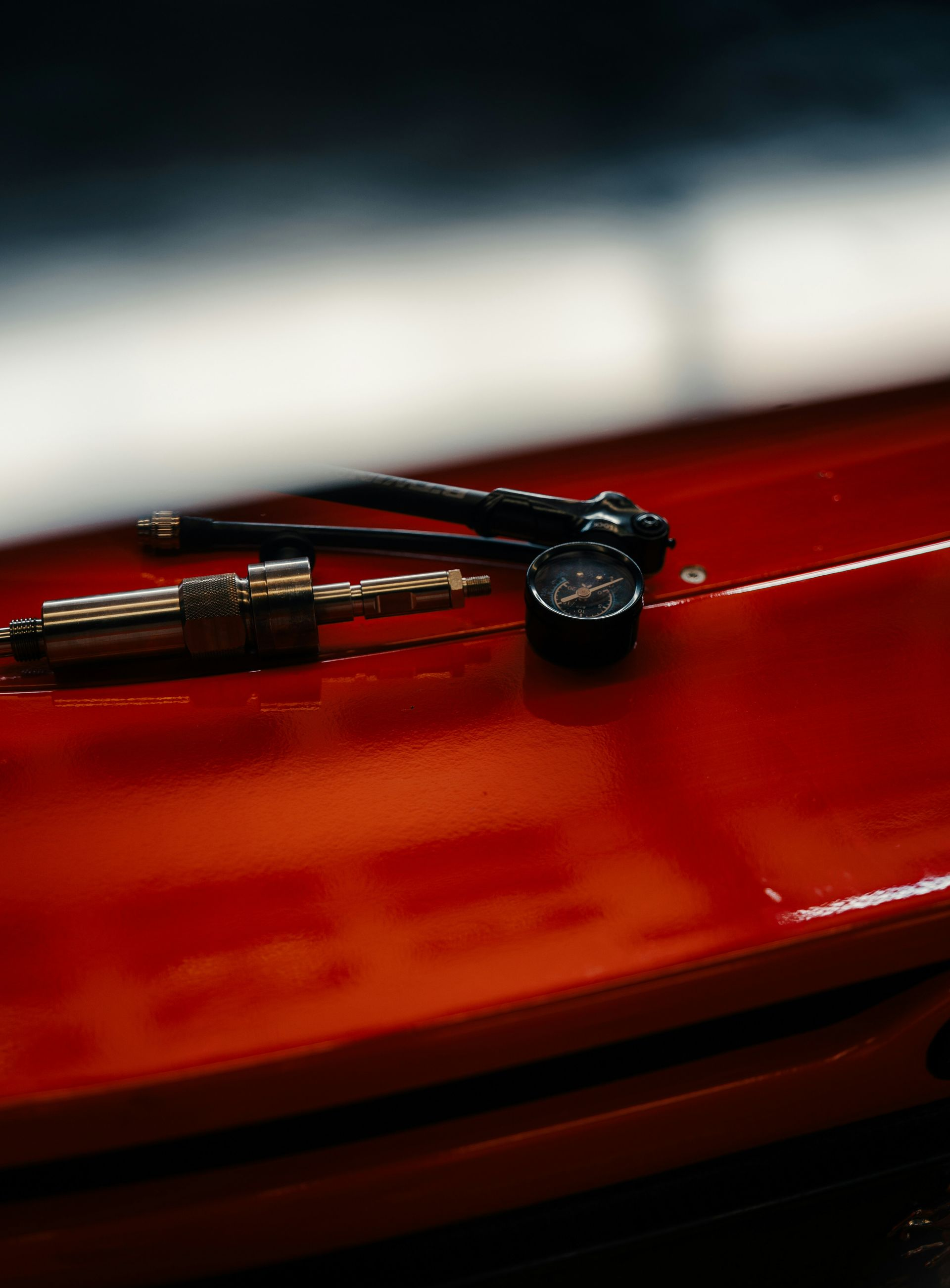 A tire pressure gauge and a valve stem tool rest on the bright red, glossy surface of a car hood.