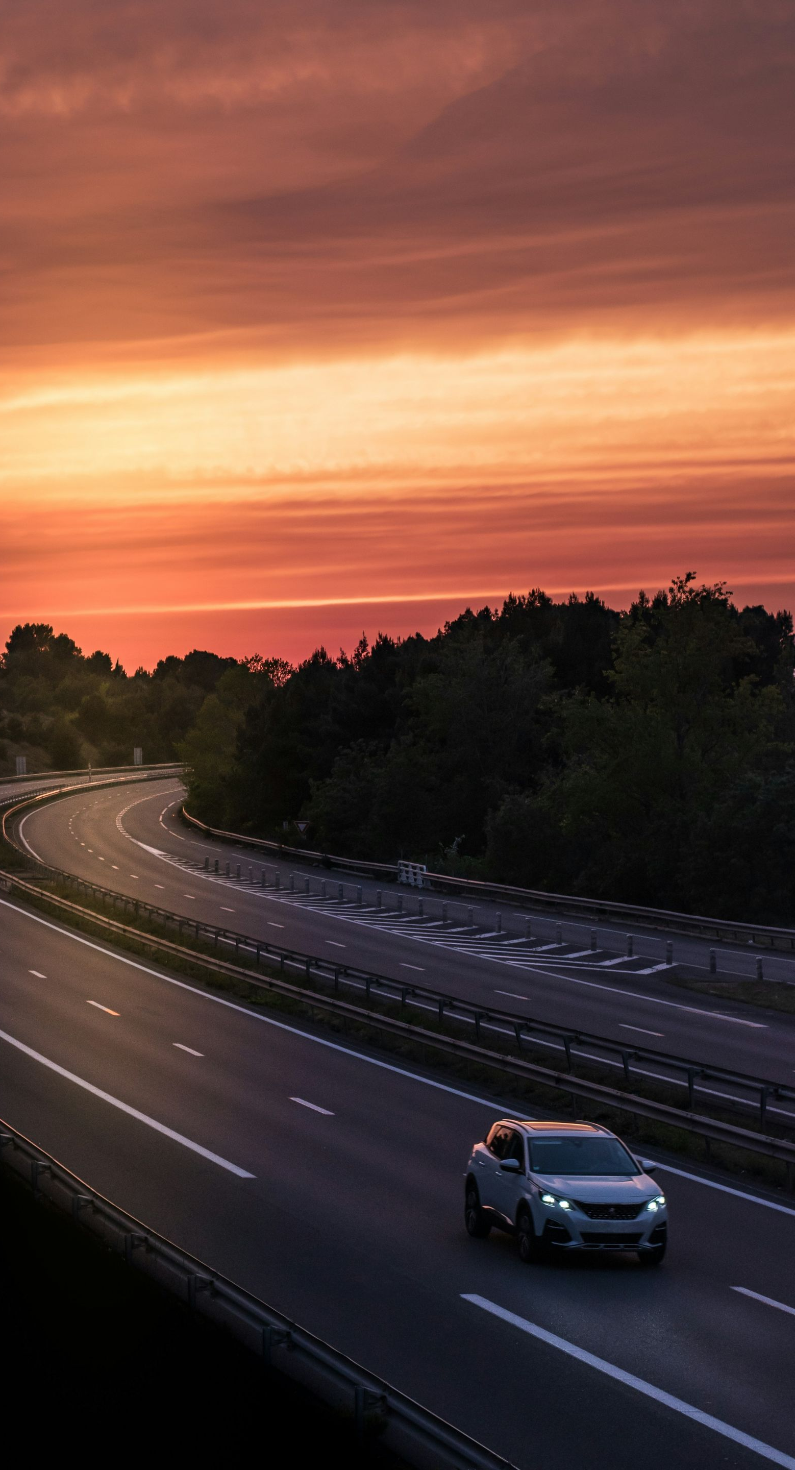 Car driving on highway at sunset. Orange and red sky above a winding road.