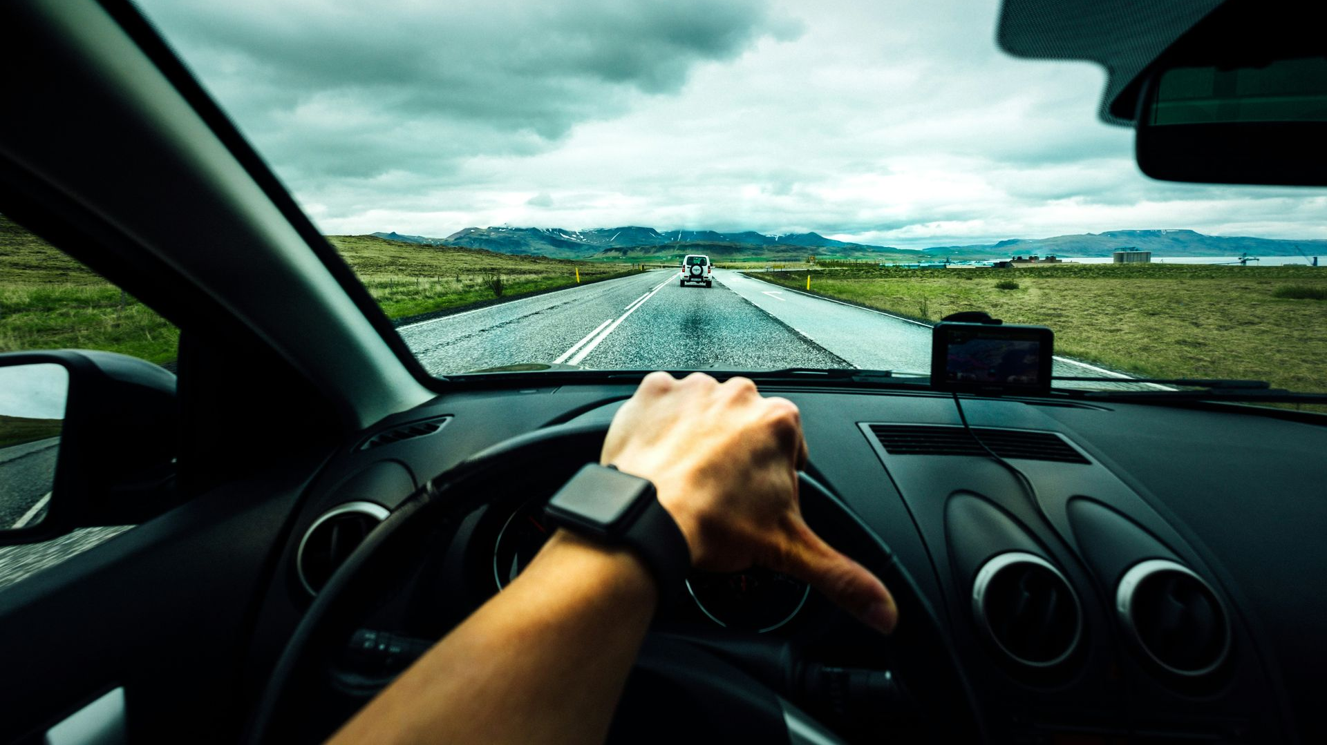 Driver’s view of a hand on the wheel on a wet road under cloudy skies