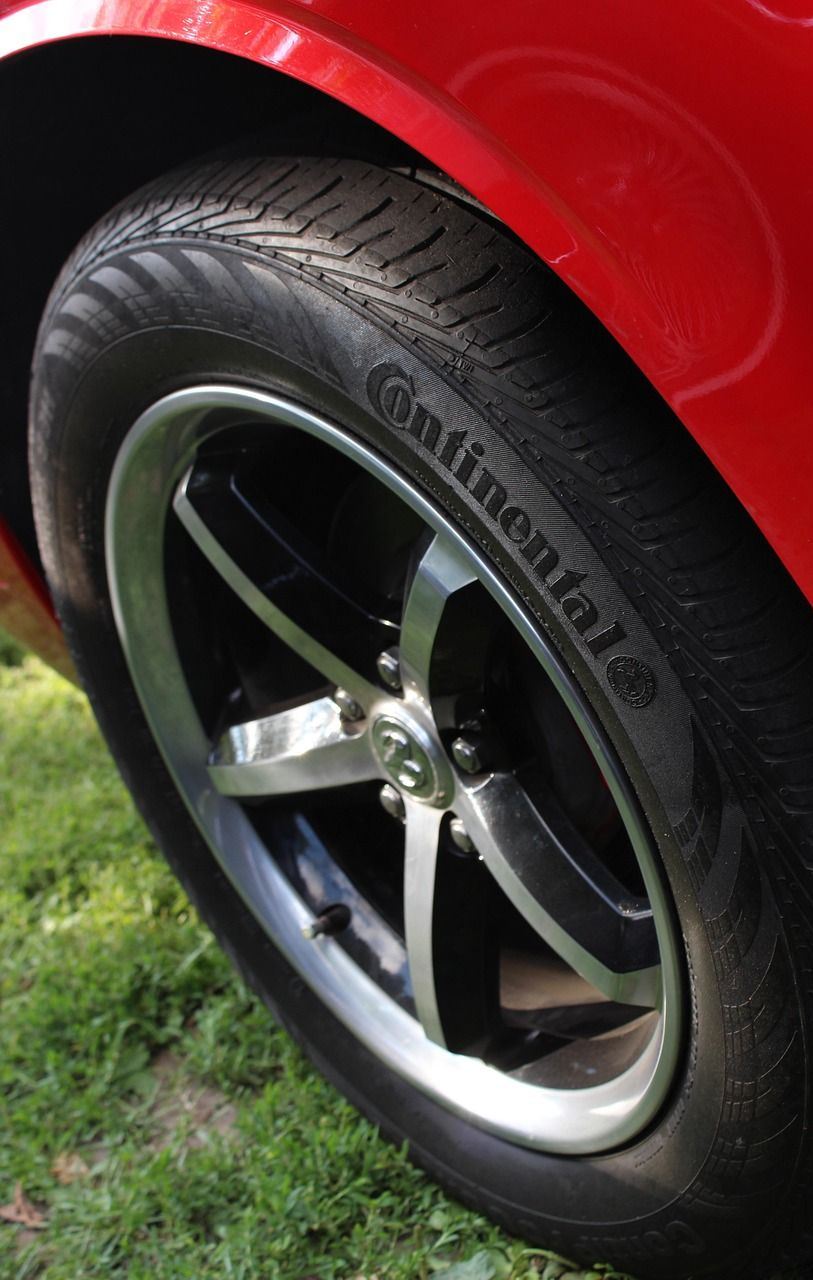 Red car wheel with Continental tire, set against a grassy background.