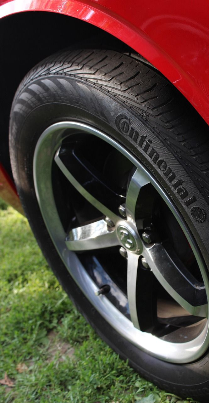 Red car wheel with Continental tire, set against a grassy background.