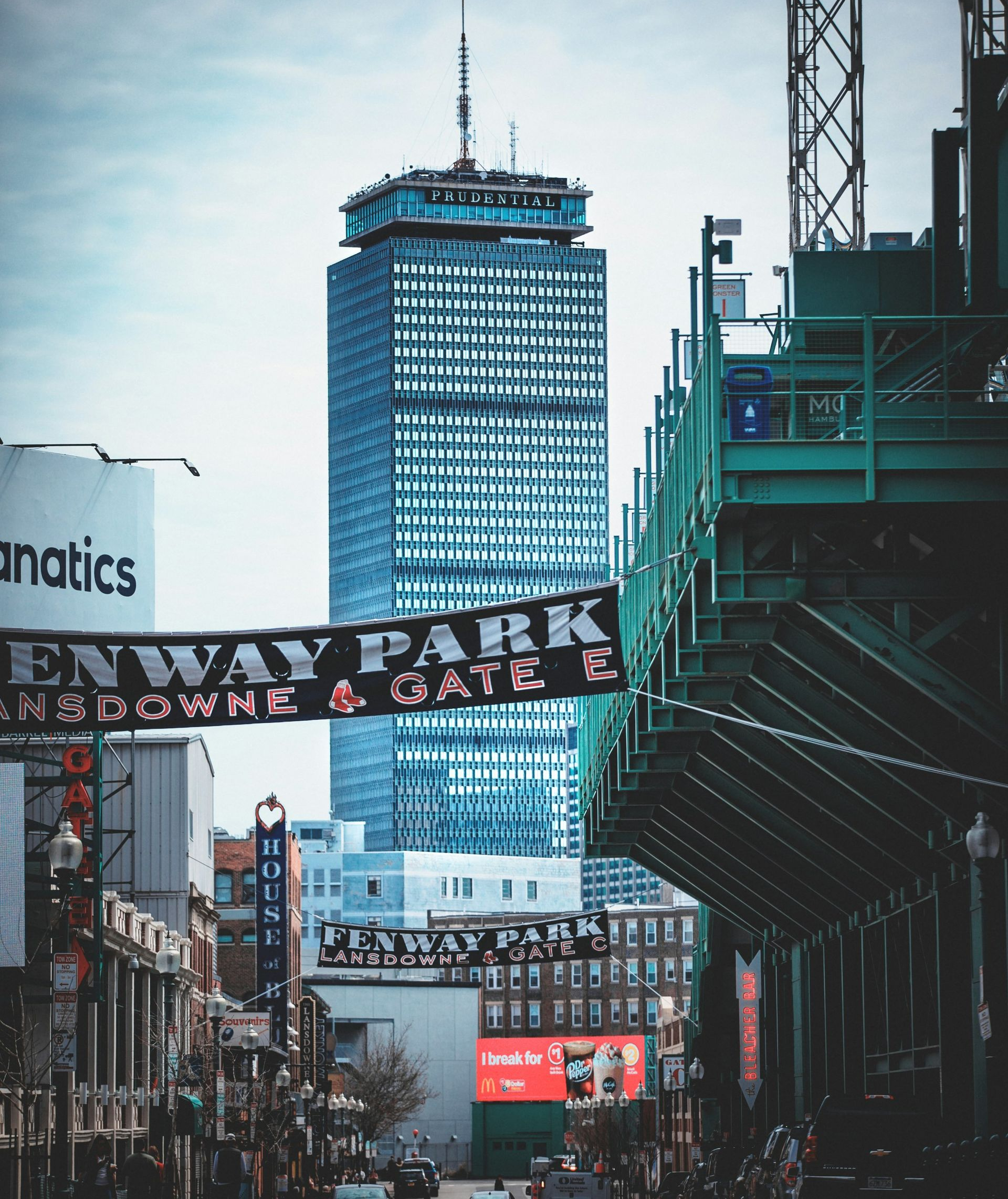 The Prudential Tower rises above Fenway Park on a street lined with banners and buildings in Boston.