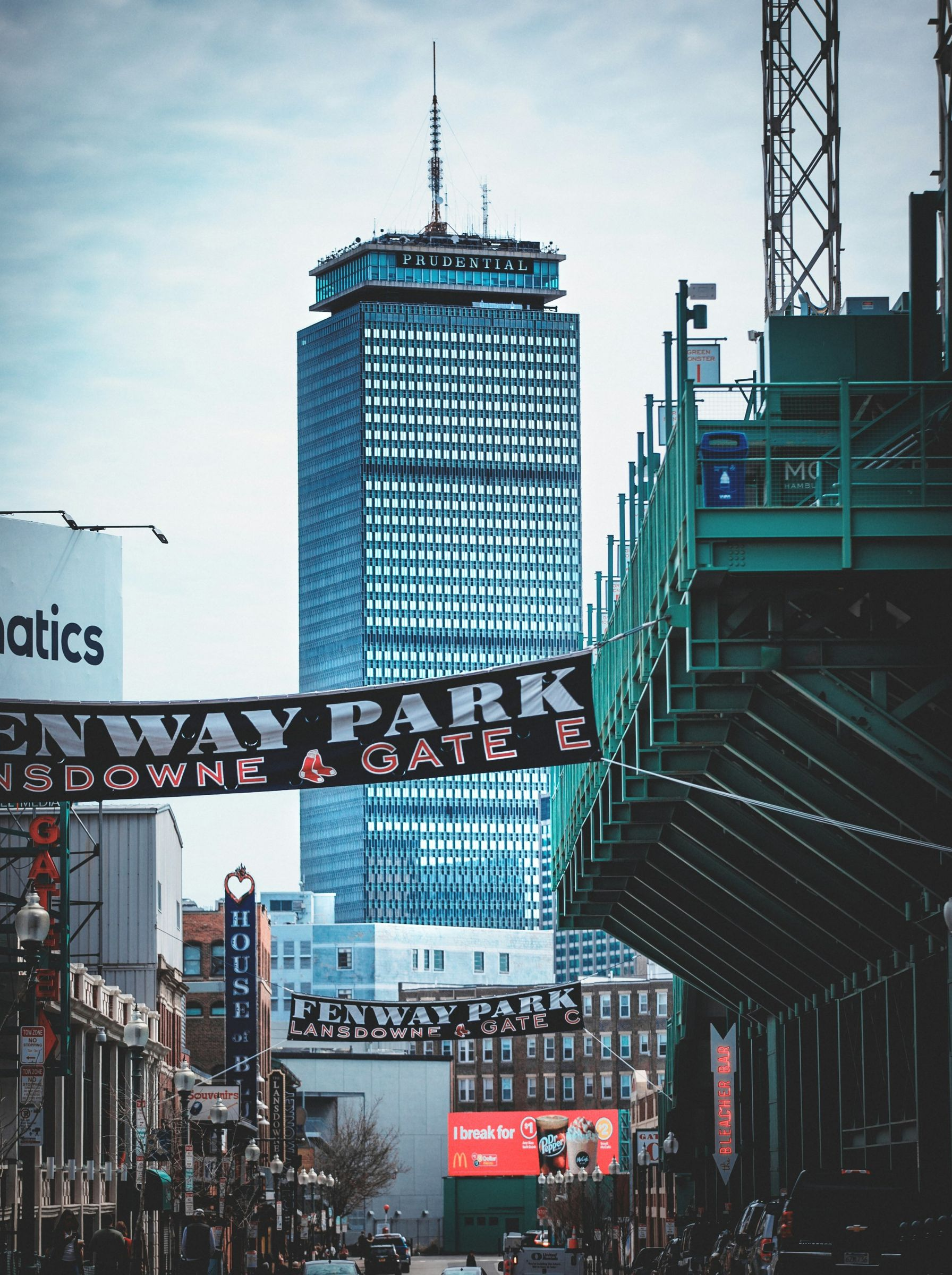 The Prudential Tower rises above Fenway Park on a street lined with banners and buildings in Boston.