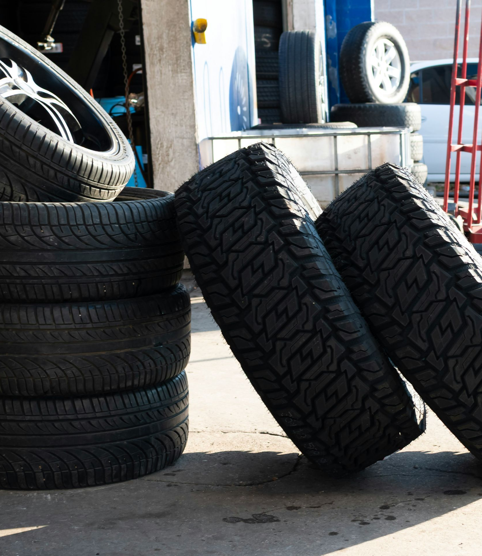 Tires stacked and leaning in a garage setting, sunlight.