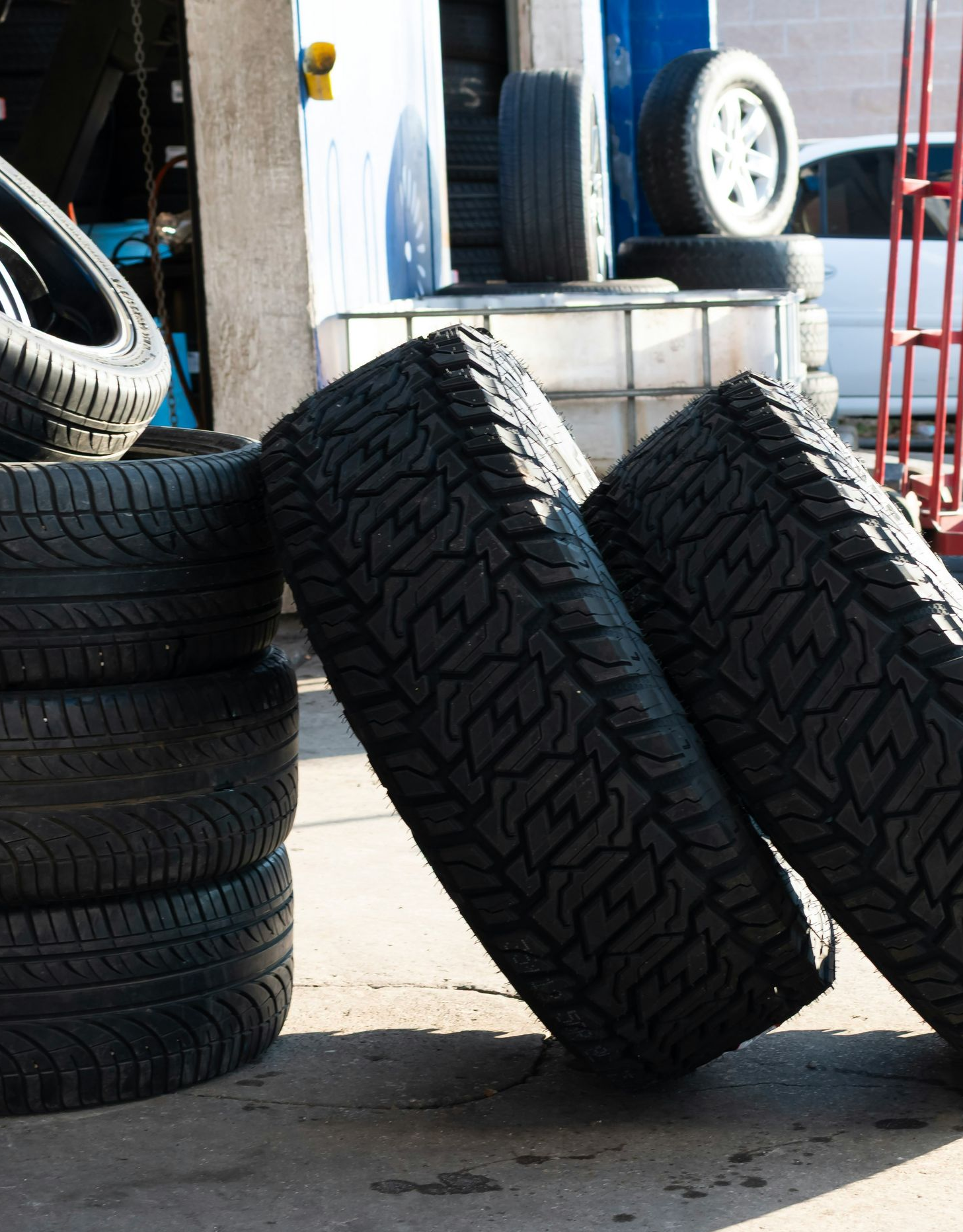Tires stacked and leaning in a garage setting, sunlight.