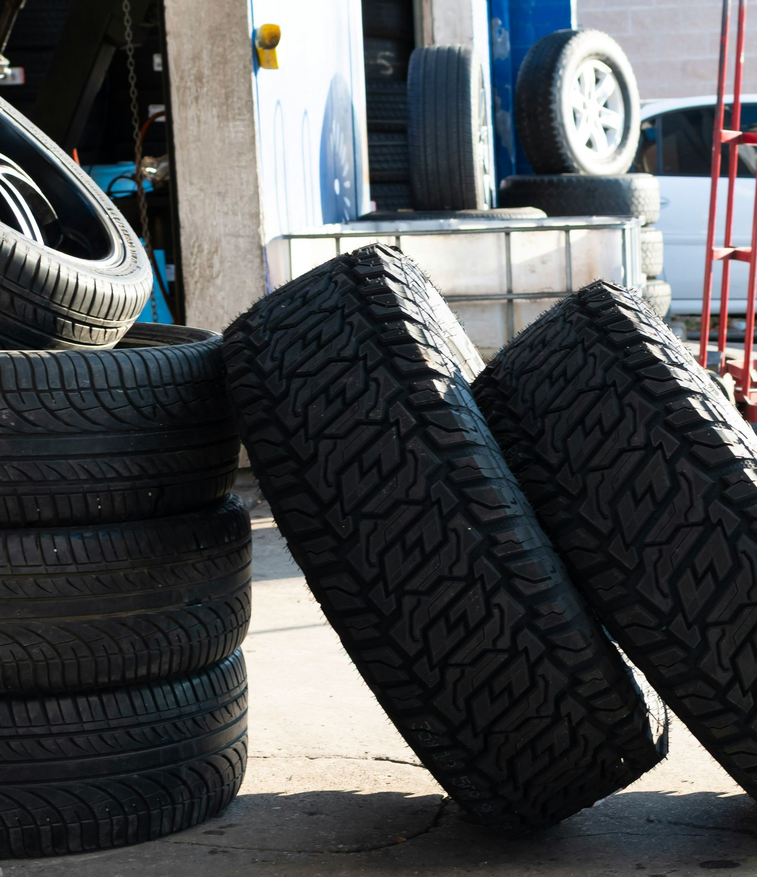 Tires stacked and leaning in a garage setting, sunlight.