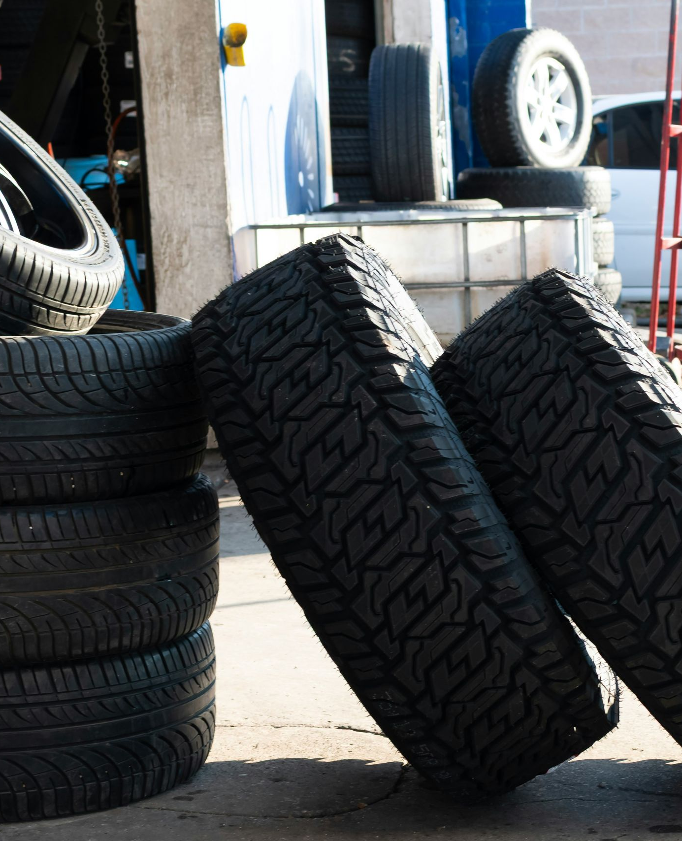 Tires stacked and leaning in a garage setting, sunlight.