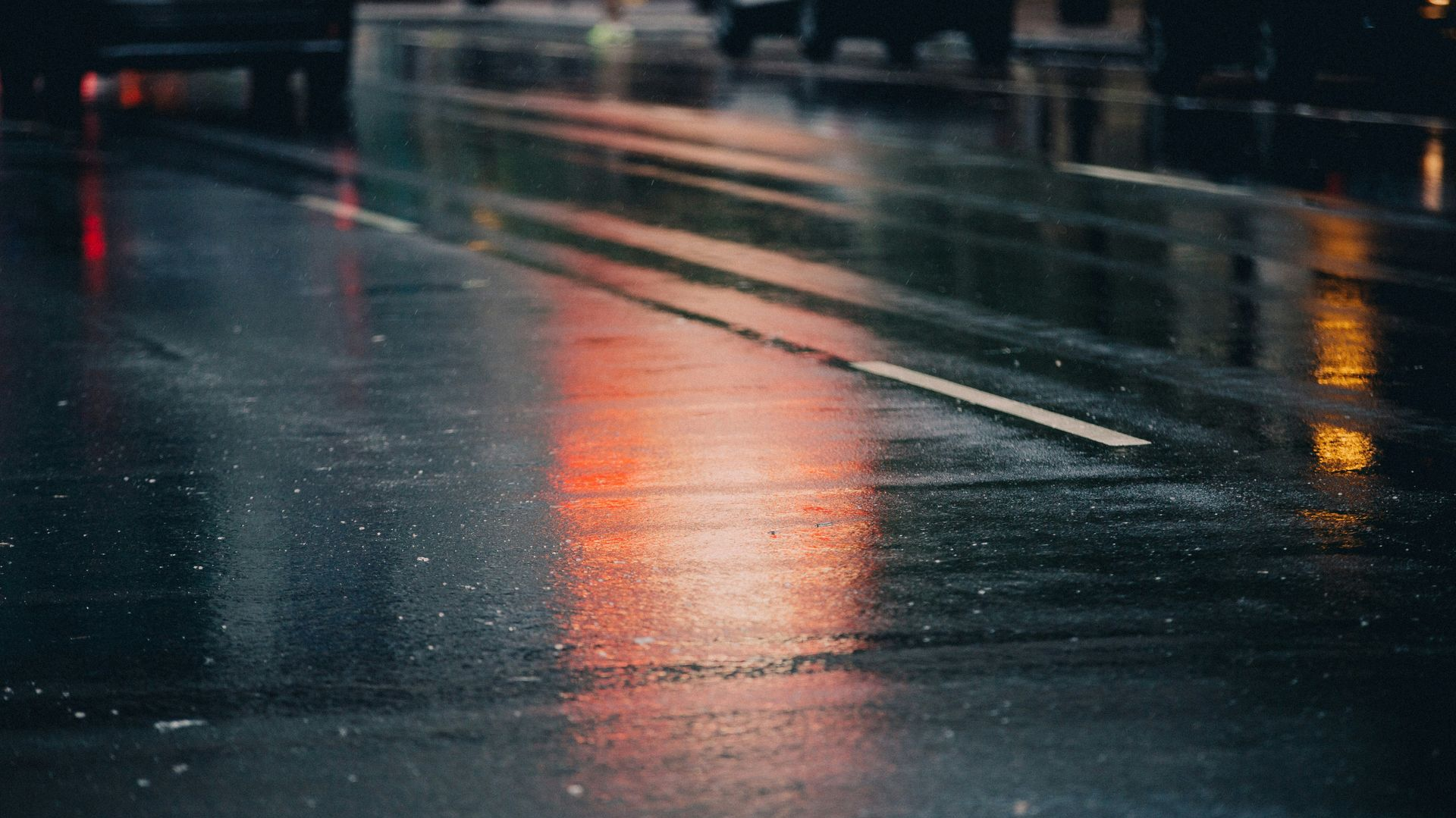Rainy street at night with wet pavement reflecting orange lights