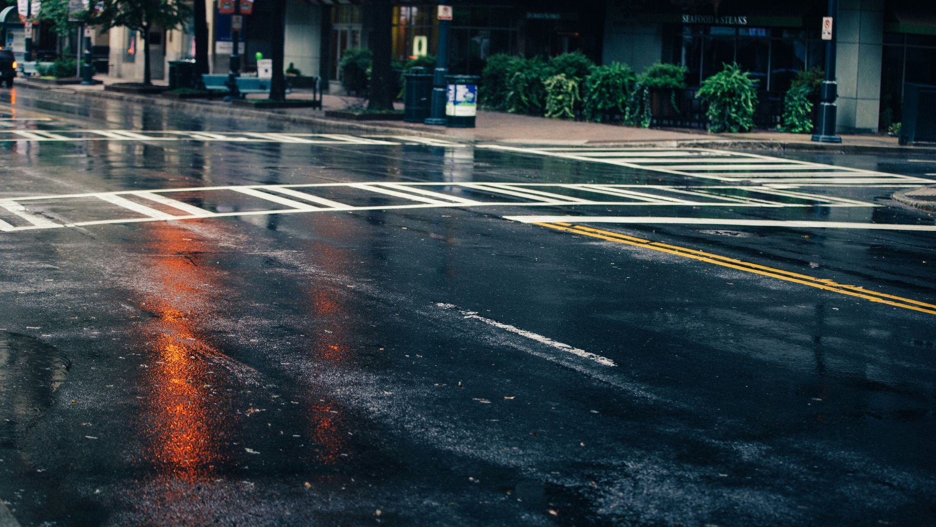 Rain-slick city street with reflective pavement and crosswalk lines at dusk
