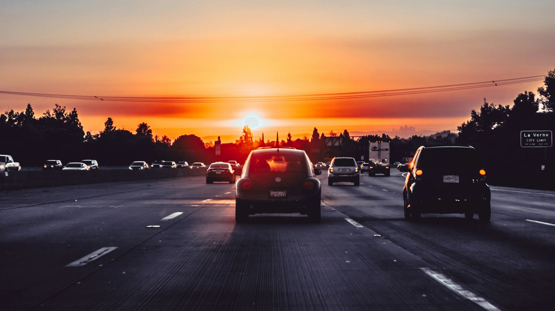 Cars driving on a highway at sunset, with orange light on the horizon.