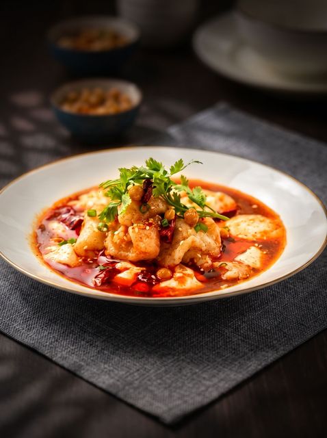 Steaming saucy dish garnished with herbs on a white plate atop a dark table setting