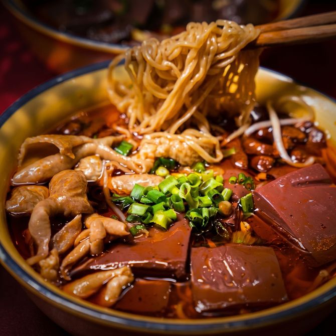 Close-up of steaming noodle soup with braised meat, dark broth, and chopped green onions in a bowl
