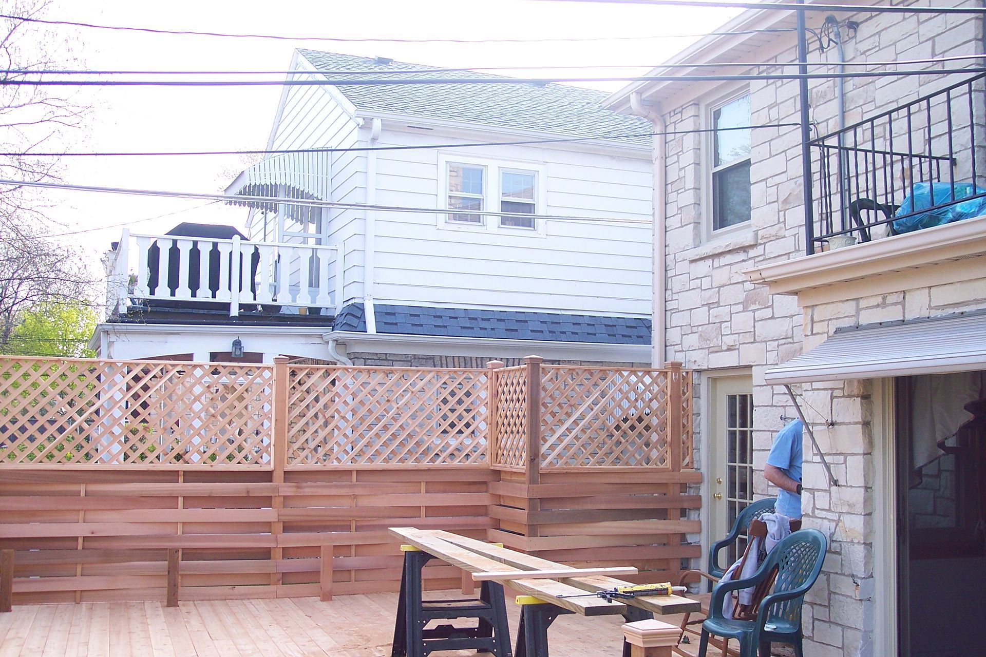 Backyard patio with wooden fence, deck, string lights, and a stone house exterior